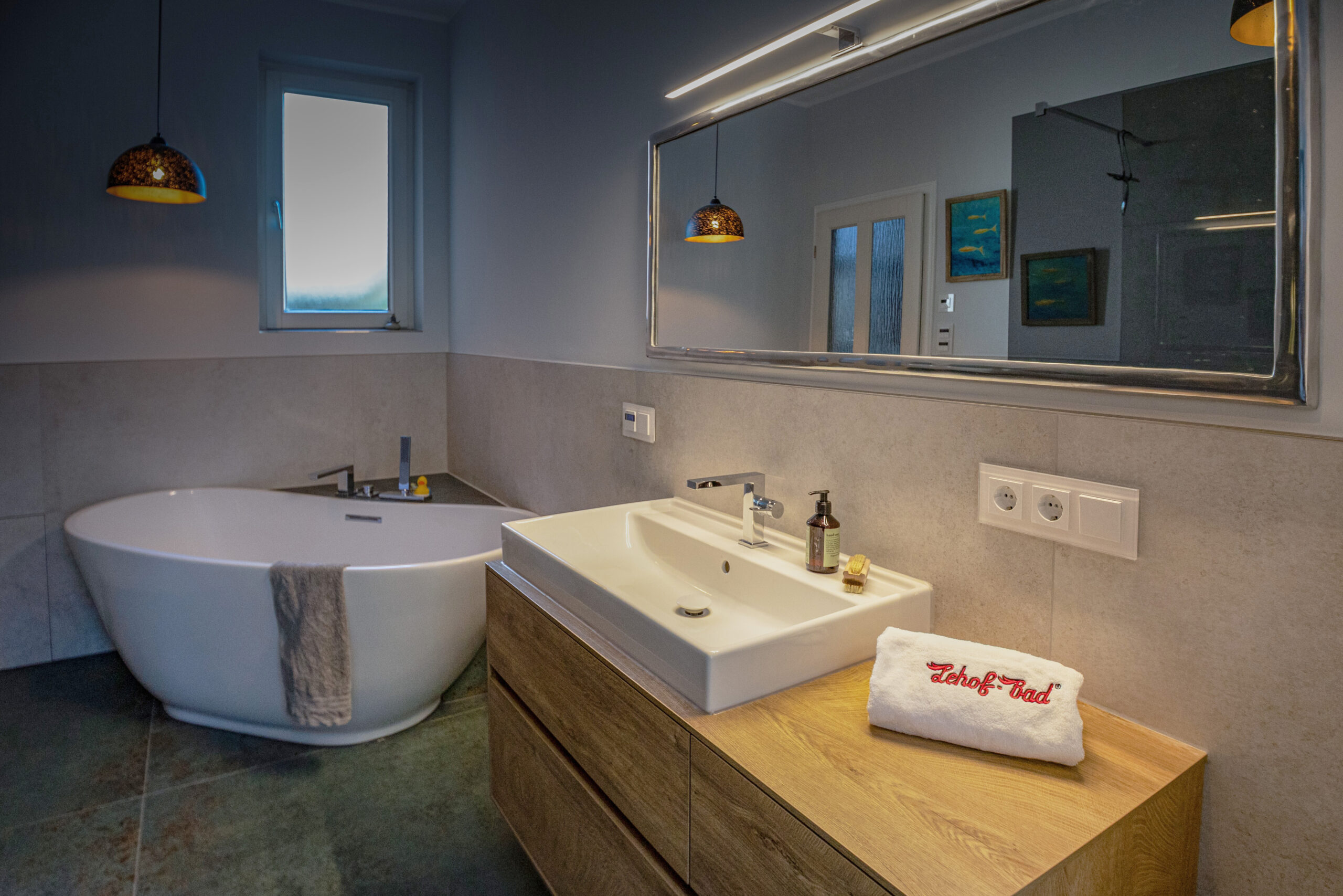 Barrierefreie Badsanierung von Lehof: Ansicht einer modernen, freistehenden Badewanne und eines hochwertigen Holz-Waschtischs mit großem Spiegel.