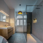 Vollständig saniertes Badezimmer von Lehof mit bodengleicher Walk-in-Dusche, Glasabtrennung, einem modernen Holz-Waschtisch und dunklen Bodenfliesen. Titel: Komplett-Badsanierung-Lehof-Walk-In-Dusche